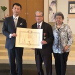 林大使から叙勲叙勲された肥田医師（中央）と文子（あやこ）夫人（提供写真）