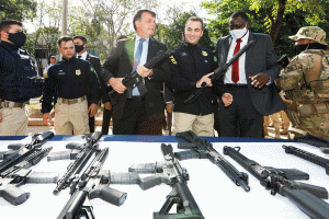 警察が犯罪者組織から押収した銃を手に取るボルソナロ大統領（Carolina Antunes/PR e Polícia Civil/RJ）