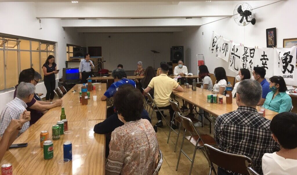 忘年会で挨拶する小林氏（左奥）