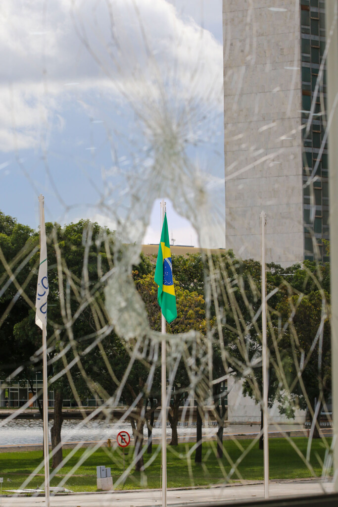 破壊された大統領府のガラス越しに見えるブラジル国旗（Fabio Rodrigues-Pozzebom/Agência Brasil）