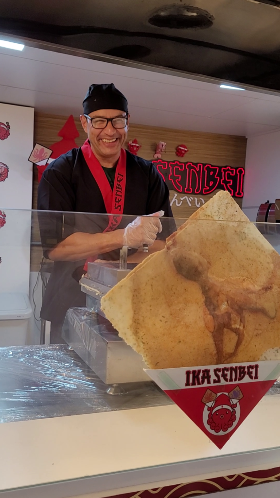 手前がタコのセンベイ。ブラジル初専門店「ＩＫＡ ＳＥＮＢＥＩ」、奥が従業員のマルコスさん