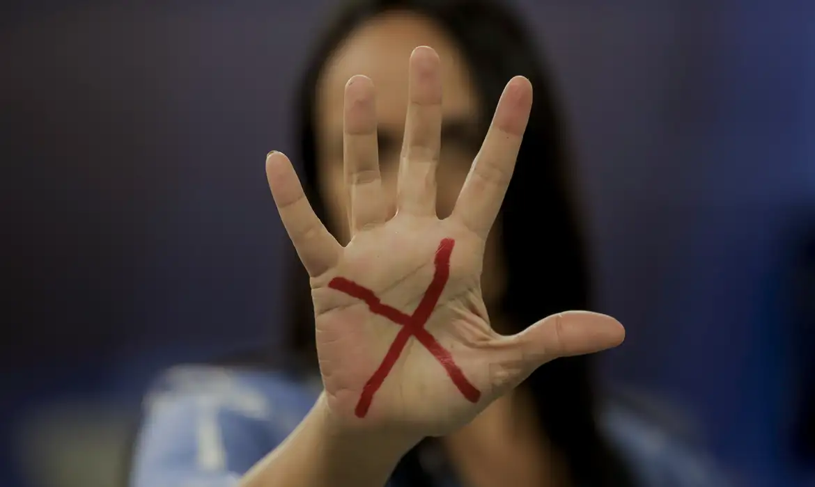 女性への暴力拒否を示すサインを見せる女性（© Joédson Alves/Agência Brasil）
