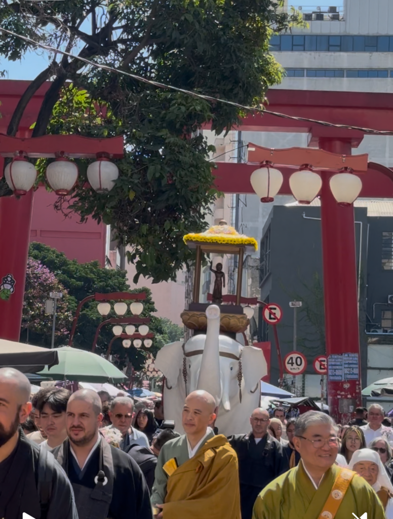 鳥居の下を行進する釈迦像を載せた白い象と僧侶ら