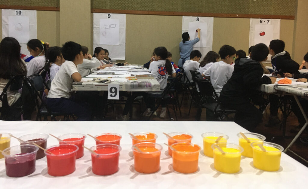 用意された絵具と手本を見ながら描く生徒たち